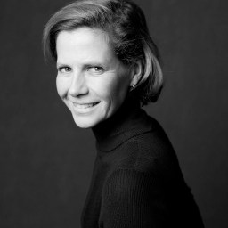 Black and white portrait of a woman with short hair wearing a dark turtleneck, smiling and looking slightly over her shoulder against a plain background.
