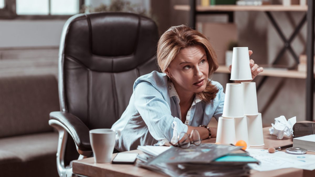 A woman with no inspiration stacks cups on her desk.