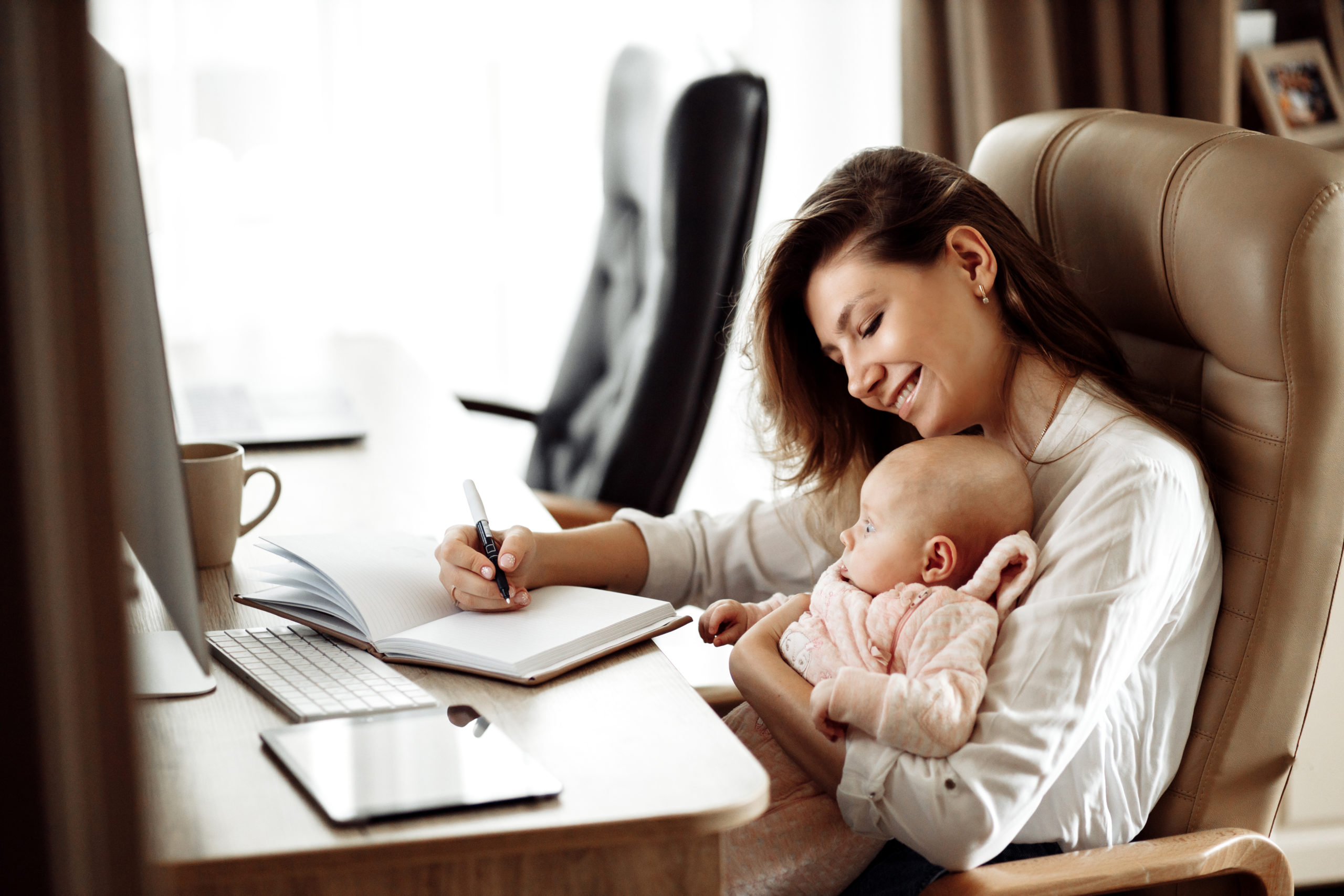 A working mom makes notes while holding her daughter.