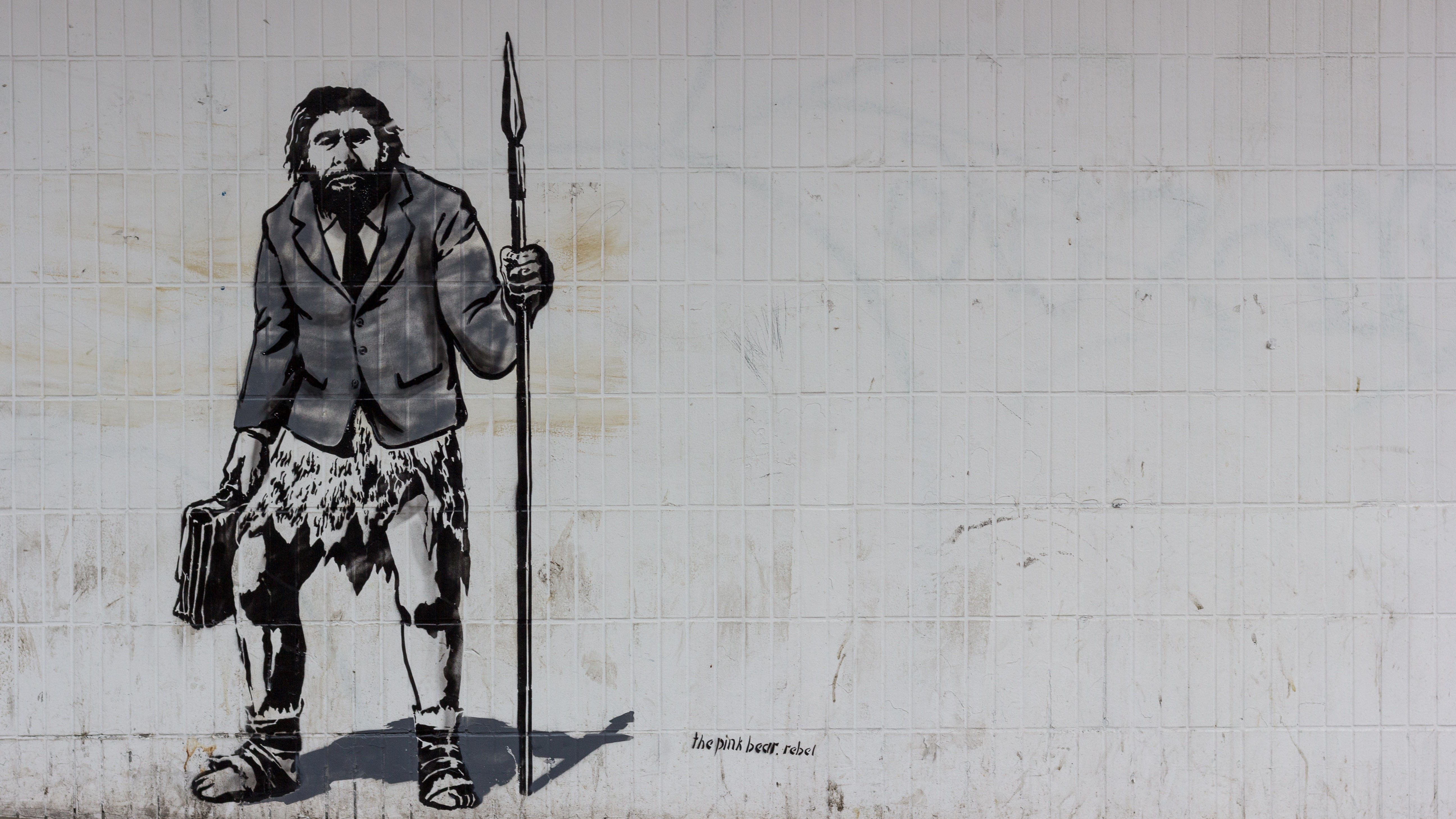 A Neanderthal man holding a briefcase in one hand and a spear in the other.