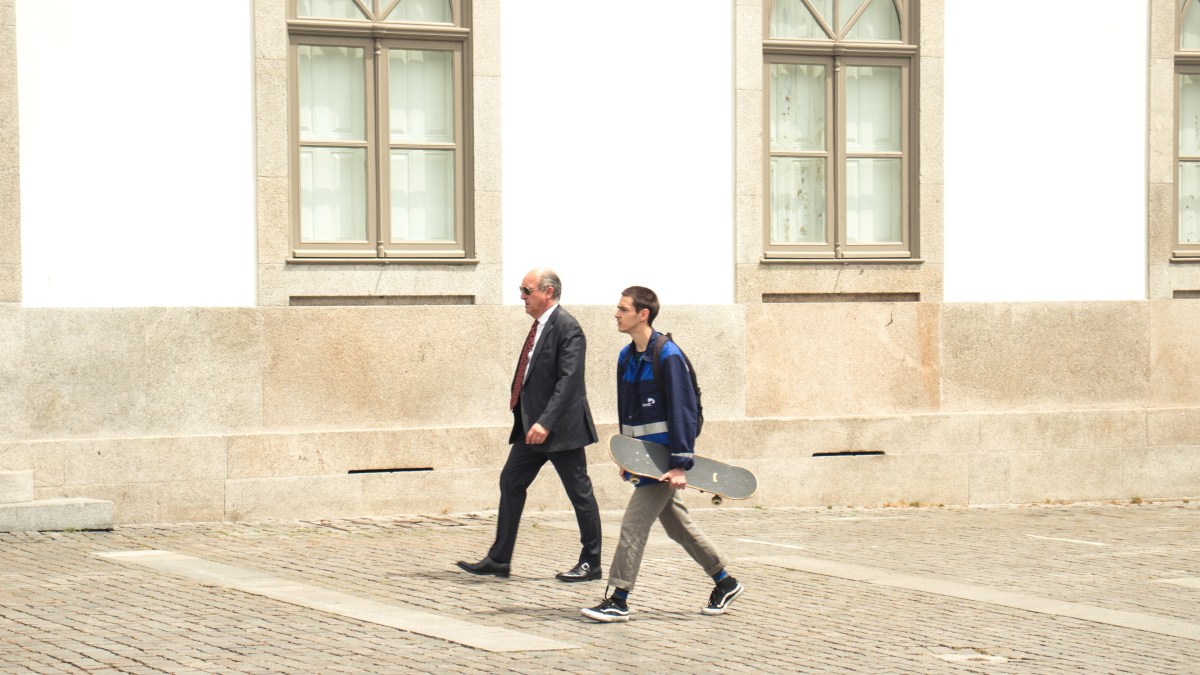 A man in a suit walks next to a teenage boy carrying a skateboard, illustrating life stages.