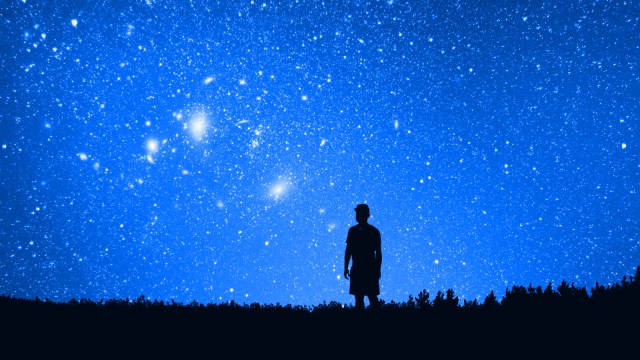 Silhouette of a person standing on a field at night, gazing at a clear sky filled with stars and glowing celestial objects, evoking the wonder described by Jim Al-Khalili.