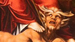 A horned, fanged figure lies on the ground with a foot pressing down on its neck; red drapery is visible above.