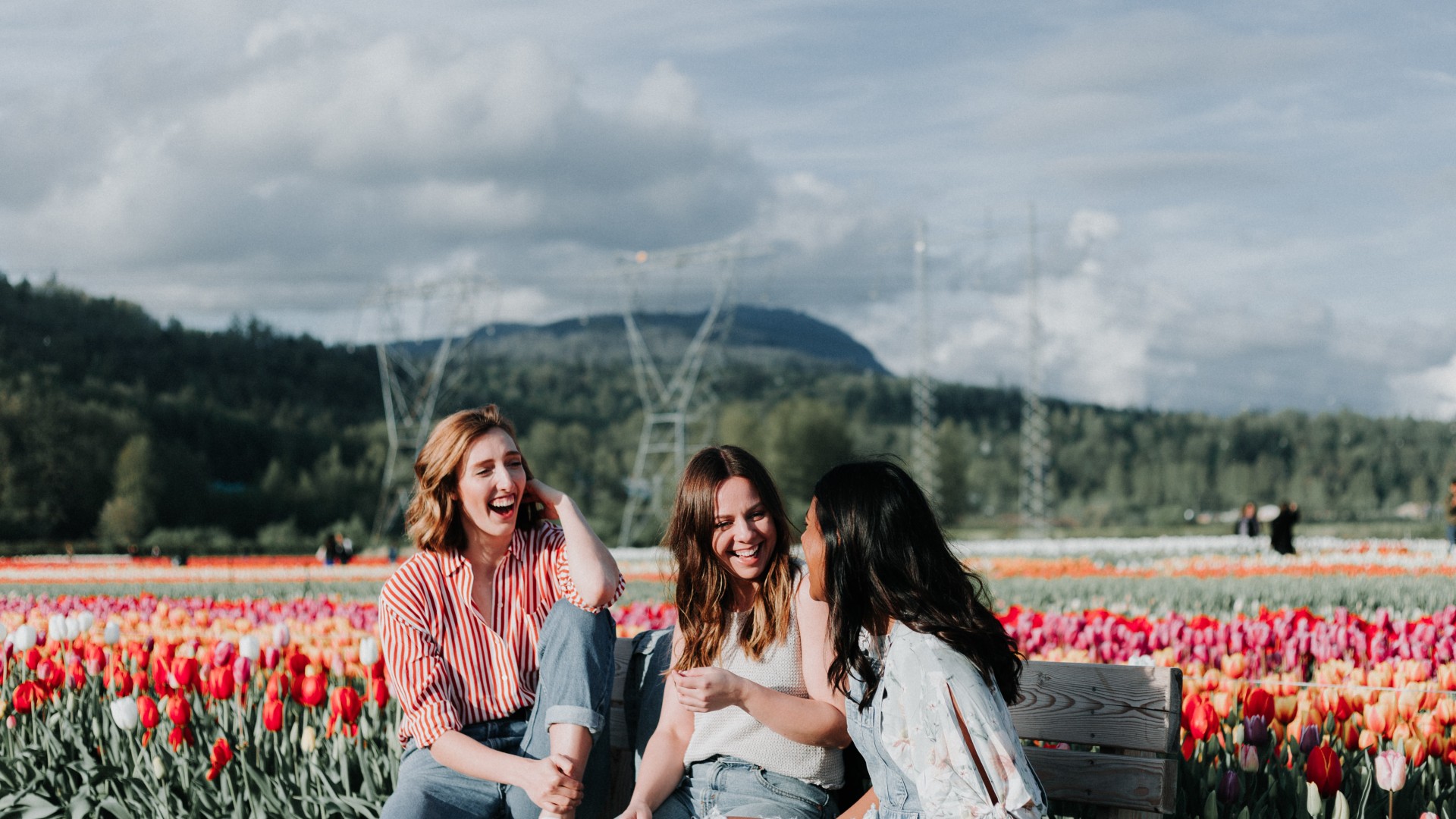 Three women share a laugh while visiting a tulip field.