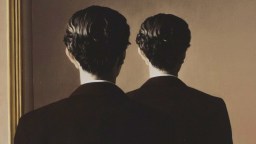 A man in a suit stands facing a mirror, but the reflection shows the back of his head instead of his face.