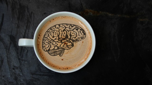 A cup of coffee with a brain silhouette drawn on the foam.