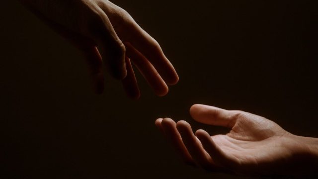 two hands reaching towards each other in the dark.