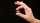 A hand pinches a small spiral galaxy between its fingers against a background of stars in space.