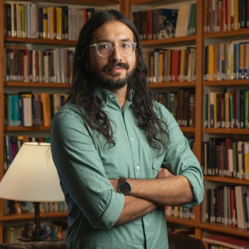 a man with long hair and glasses standing in front of a bookshelf.