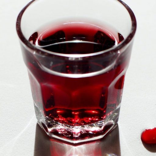 a glass of red liquid sitting on top of a table.