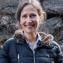 a woman in a black jacket standing in front of a rock.