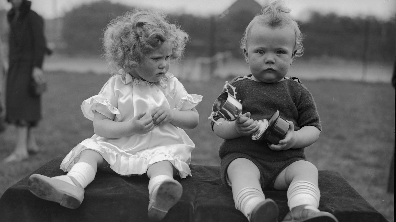 two children sitting on a blanket holding toys.