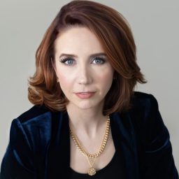 A woman wearing a black jacket and gold necklace.