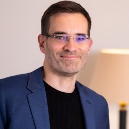 A man in glasses is smiling in front of a lamp.