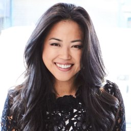 An asian woman smiling in front of a window.