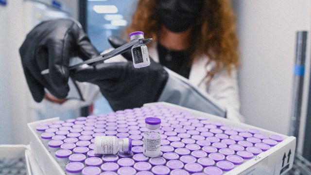 A woman holding a syringe administers an mRNA vaccine with gloves and a mask on.