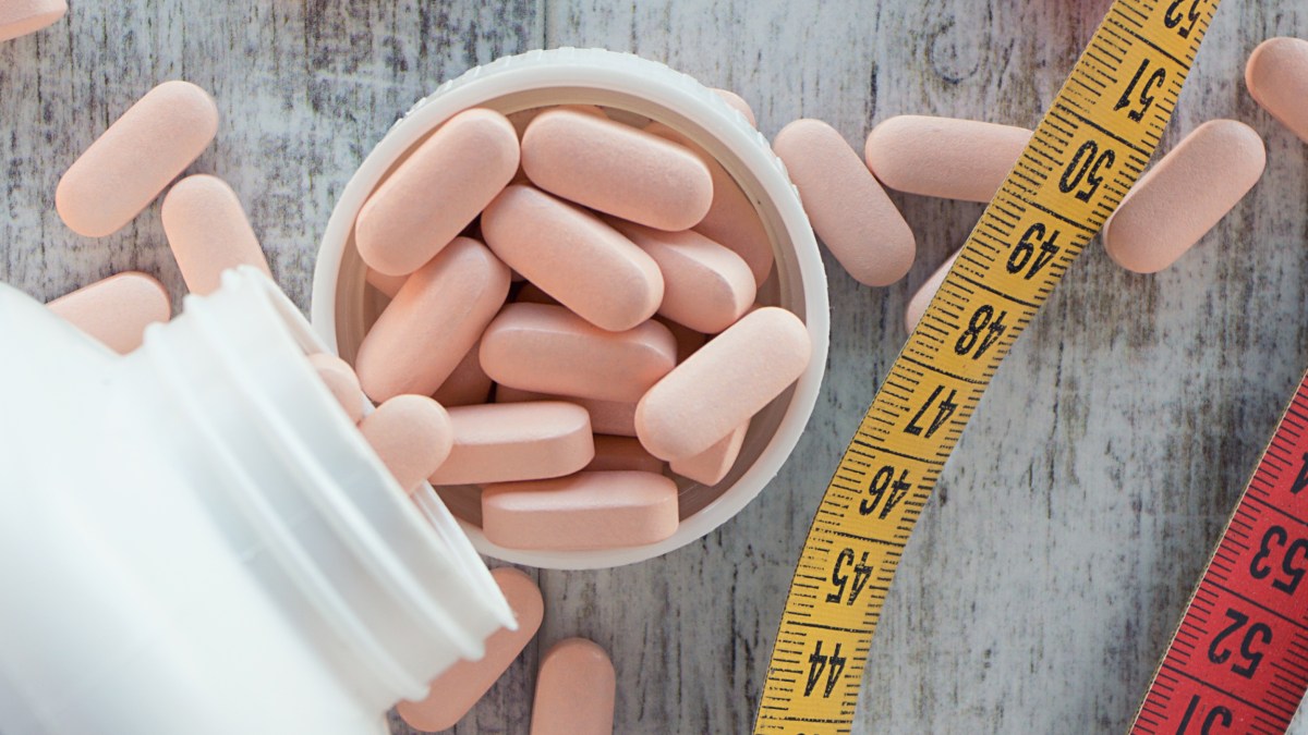 A measuring tape alongside a bottle of exercise pills on a wooden table.