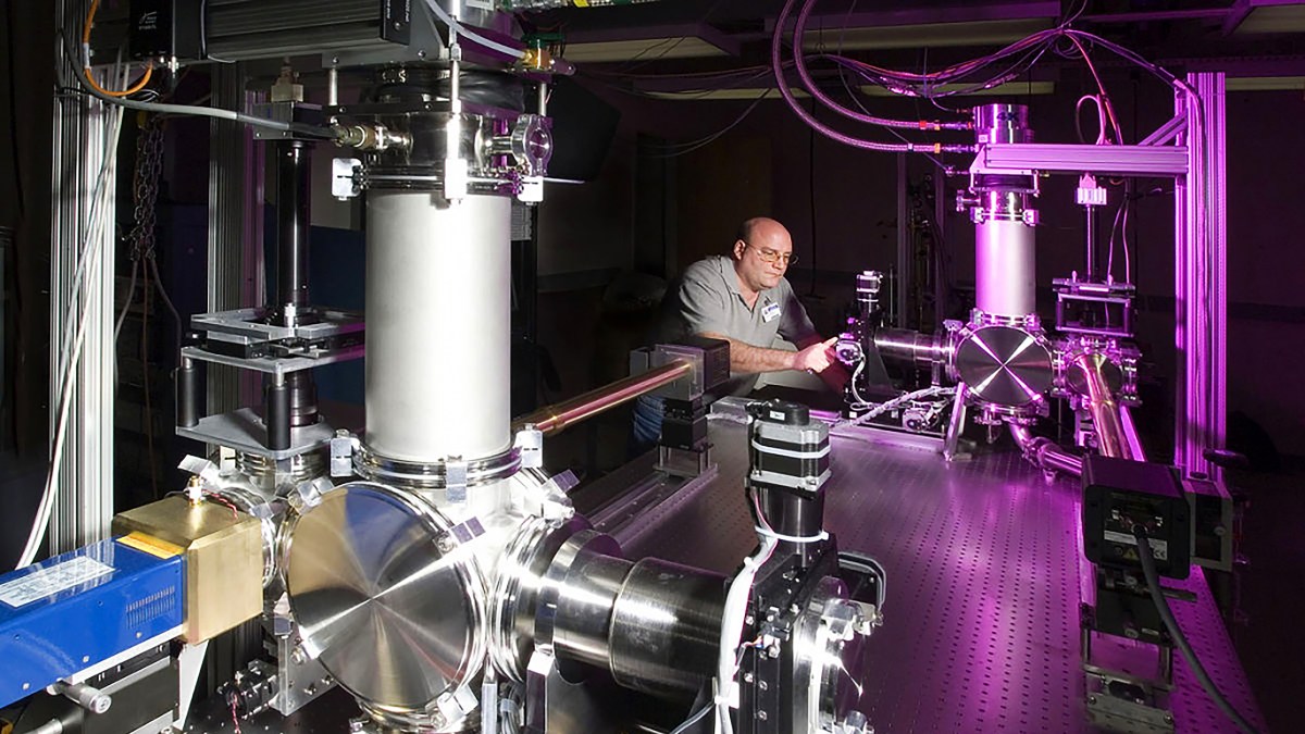 A man is working on a machine in a lab, using laser technology to apply precise pressure.