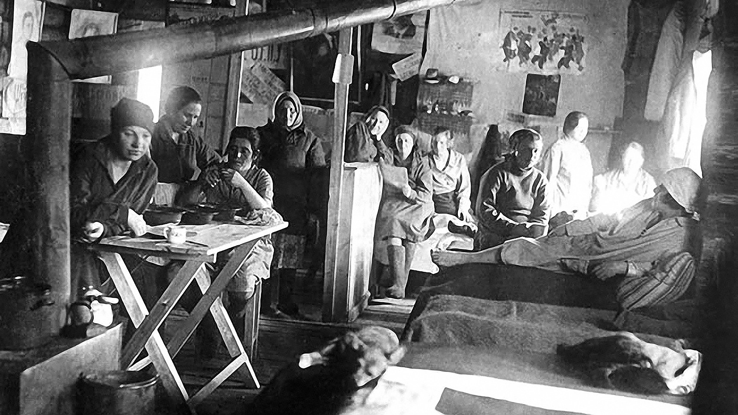 A group of people sitting around a table in a room, engaged in conversations amidst an air of exile.