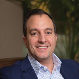 A smiling man in a blue suit sitting on a couch.