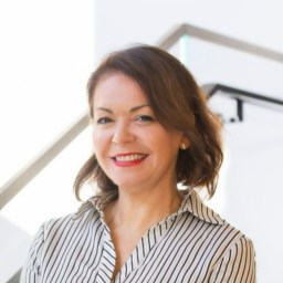 A woman in a striped shirt smiling in front of stairs.
