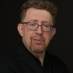A man with glasses and a beard is posing for a photo.