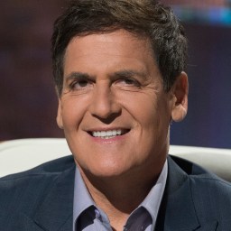 A smiling man in a suit sitting on a chair.