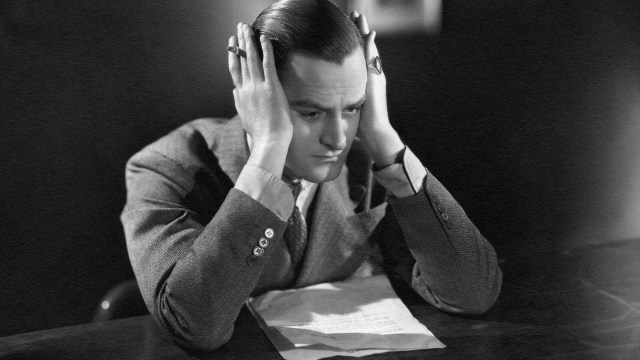 A man sitting at a desk in isolation, with his hands on his head.