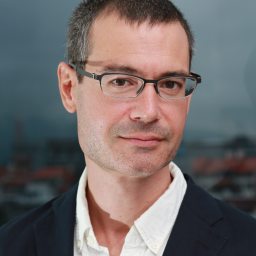 A man in glasses is standing in front of a city.