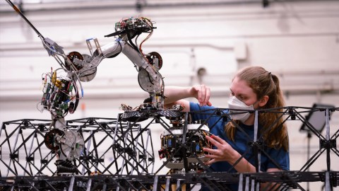 A woman is working on a robot in a factory.