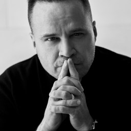 A black and white photo of a man posing with his hands in his pockets.