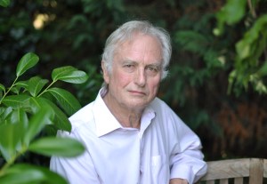 Elderly individual with white hair and a white shirt sits outdoors surrounded by lush green foliage.