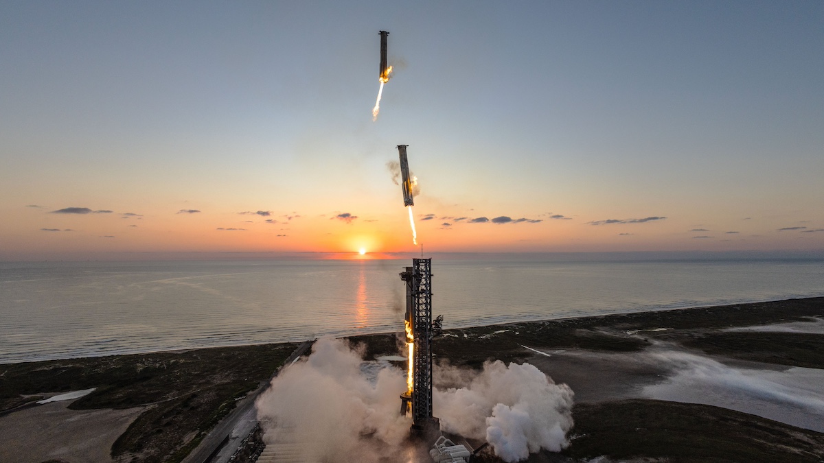 A rocket launches at sunrise by the ocean, with flames visible beneath. Two booster stages separate mid-air, leaving trails of smoke as they fall back to the ground.