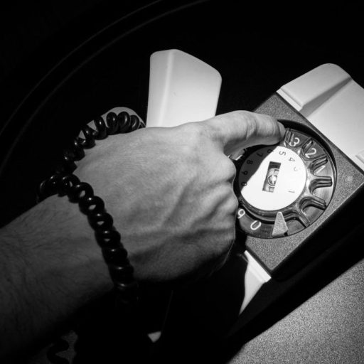 A hand with emotional intelligence dials a vintage rotary telephone, its coiled cord adding to the nostalgia of the black-and-white scene.
