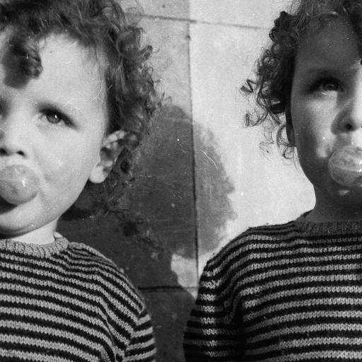 Two young children with curly hair in striped sweaters enjoy lollipops, showcasing the whimsical nature of genes and behavior. The black-and-white photo gives a nostalgic feel.