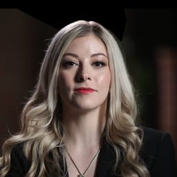 A woman with long blonde hair wearing a black suit and necklace.