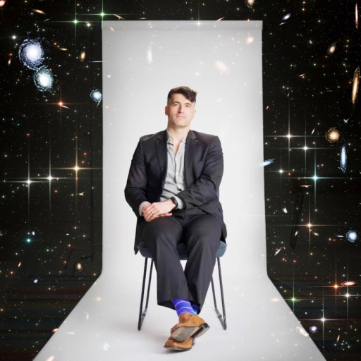 A person in a suit sits on a chair against a cosmic background with galaxies and stars.