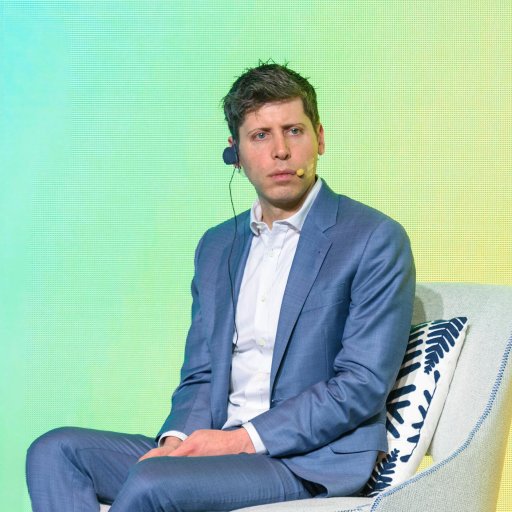 A man in a suit sits on a stage chair with a headset, set against a vibrant green background, ready to discuss the latest advancements at OpenAI.