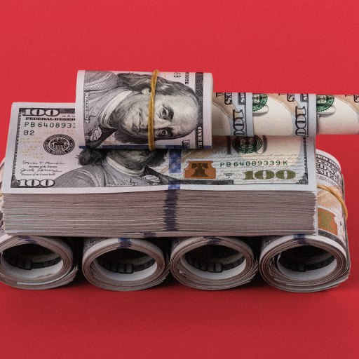 A miniature tank made from rolled and stacked U.S. hundred-dollar bills is displayed on a red background.