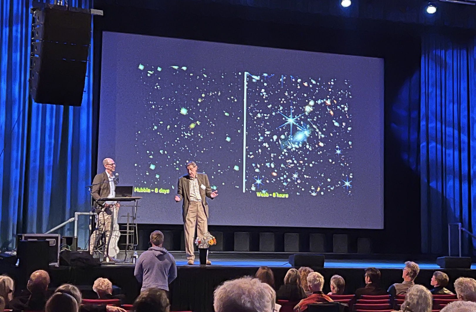 Two presenters on stage discuss a space-themed presentation with NASA's most important images in history displayed on a large screen. Audience members watch from seated positions, captivated by the stunning Hubble images of stars.