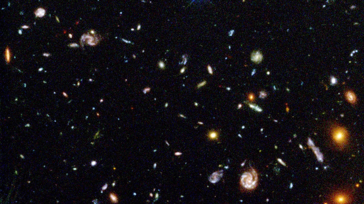 A vast view of deep space, captured in one of NASA's most important images, displays numerous galaxies of varying shapes and colors against a dark backdrop scattered with distant stars.