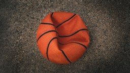 A deflated basketball lies on rough, textured ground.