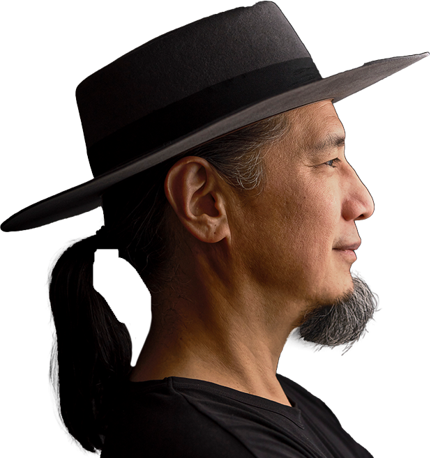 A man with a black ponytail and goatee wearing a wide-brimmed hat and black shirt is shown in profile against a dark background.