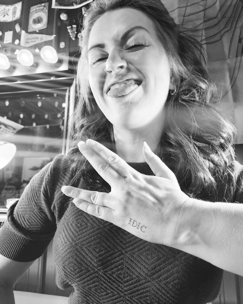 A woman makes a playful face while holding up her hand in the Vulcan salute, "IDIC" tattooed on her hand. The black and white image playfully encourages you to do your own research, much like with vaccines.