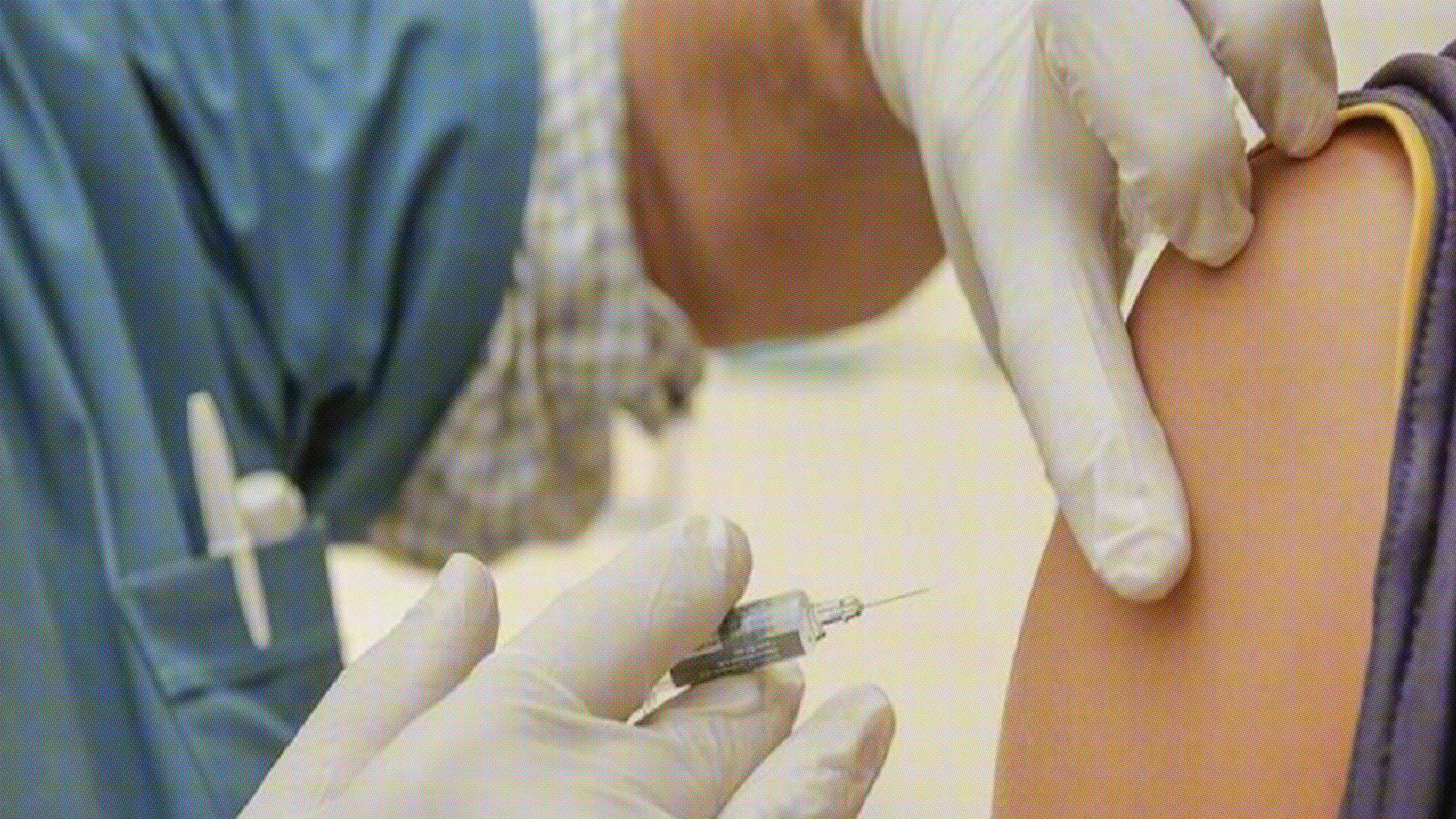 A healthcare worker wearing gloves administers an injection with a syringe into a person's upper arm, reminding us that when it comes to vaccines, do your own research and stay informed.