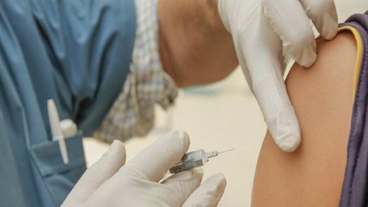 A healthcare worker wearing gloves administers an injection with a syringe into a person's upper arm, reminding us that when it comes to vaccines, do your own research and stay informed.