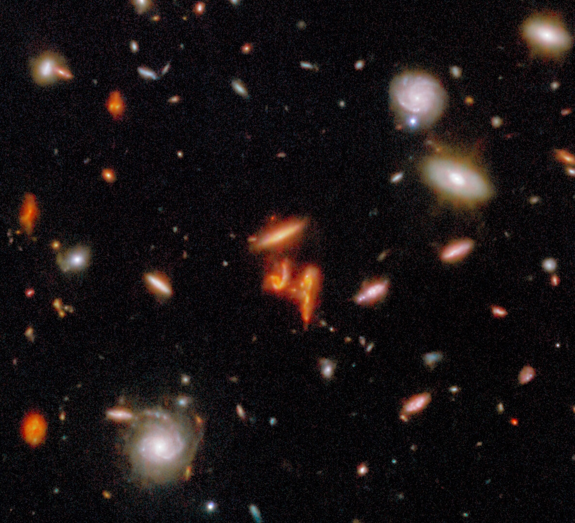 Numerous distant galaxies of various shapes and colors are scattered across a dark background in deep space.