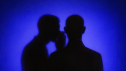 Two silhouetted figures against a blue background, with one appearing to whisper to the other.