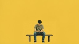 A person sits alone on a bench against a yellow background, looking down at a smartphone.