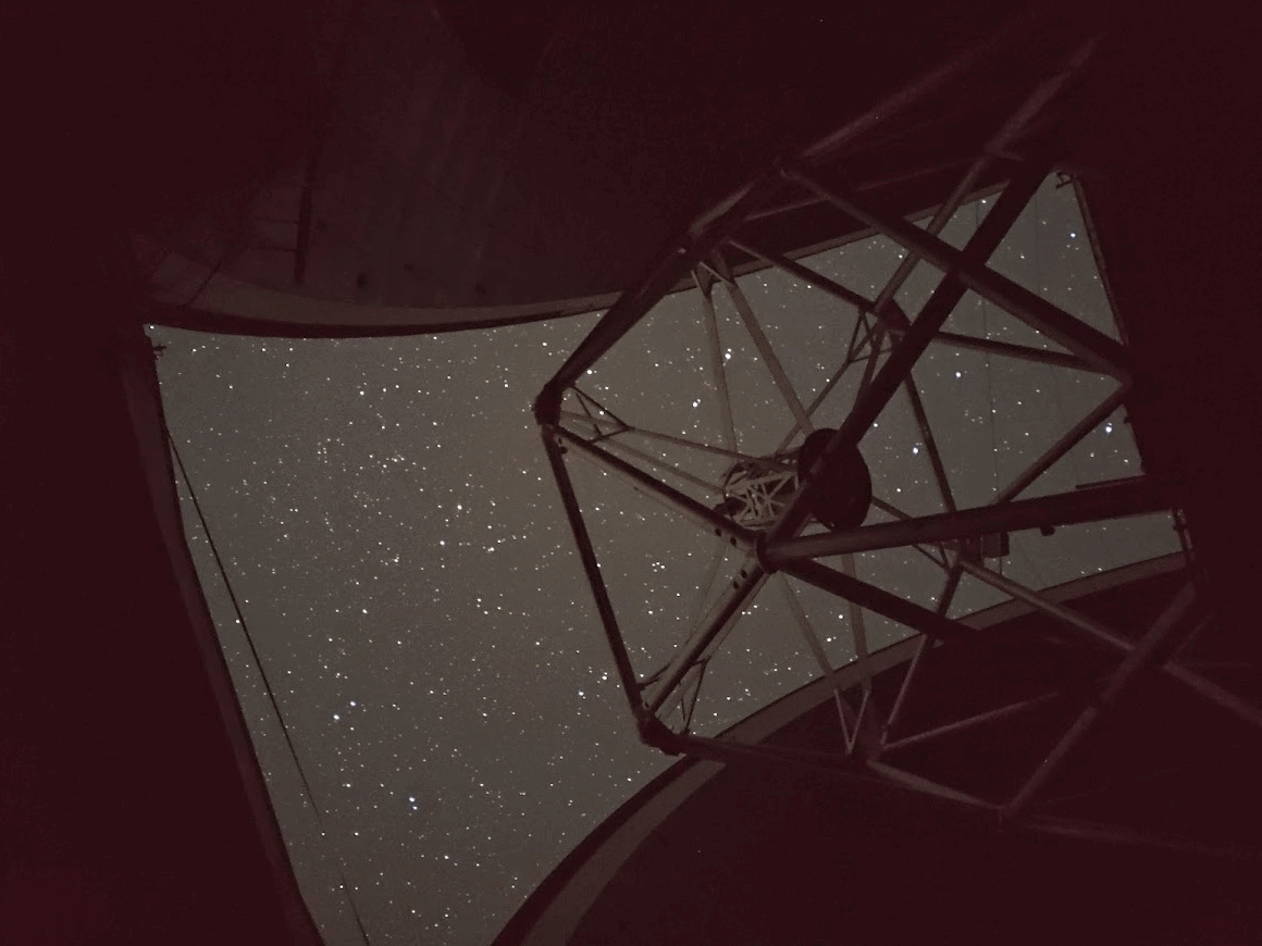 View of a star-filled night sky, which no shadows can deceive, framed by the open structure of a telescope inside an observatory dome.